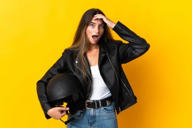 Sarı arka planda motosiklet kaskı tutan kadın yan tarafa bakarken sürpriz jest yapıyor.