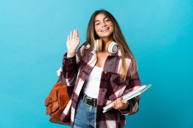 Genç bayan öğrenci, mavi arka planda izole edilmiş, mutlu bir ifadeyle selamlanıyor.
