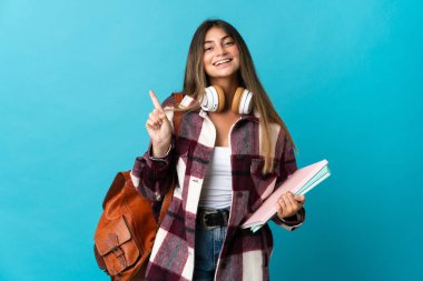 Mavi arka planda izole edilmiş genç bayan bir ürünü sunmak için kenarı işaret ediyor.