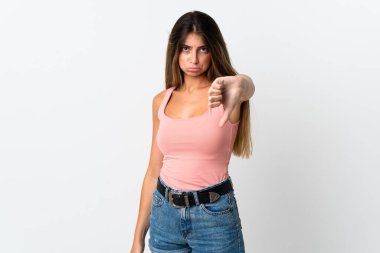 Beyaz arka planda izole edilmiş genç beyaz kadın olumsuz ifade ile baş parmağını aşağı gösteriyor.