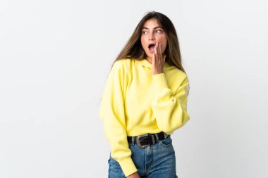 Beyaz arka planda izole edilmiş genç beyaz kadın yan tarafa bakarken sürpriz bir jest yaparak bir şeyler fısıldıyor.