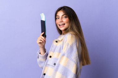 Genç beyaz kadın, mor arka planda izole edilmiş. Pasaport ve uçak biletleriyle tatilde mutlu.