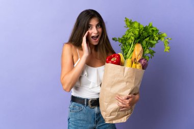 Elinde alışveriş poşeti tutan genç bir kadın. Şaşırmış ve şok olmuş bir yüz ifadesi var.