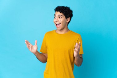 Genç Venezuelalı bir adam mavi arka planda izole edilmiş ve yüzünde sürpriz bir ifade var.
