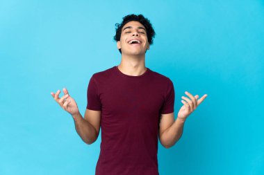 Genç Venezuelalı adam mavi arka planda izole edilmiş, çok gülümsüyor.