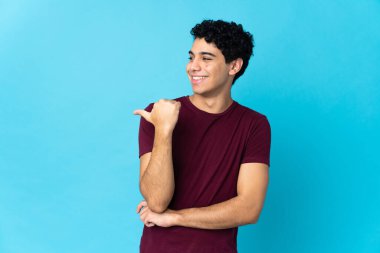 Genç Venezuelalı, mavi arka planda izole edilmiş bir adam bir ürünü sunmak için kenarı işaret ediyor.