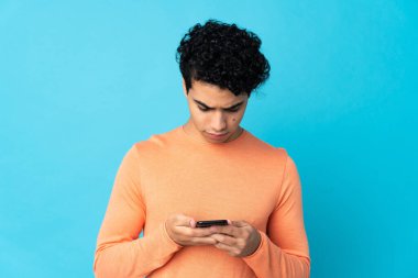 Venezuelalı adam mavi arka planda cep telefonu kullanarak izole edilmiş.