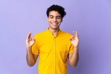 Venezuelalı genç adam, mor arka planda zen pozunda izole edilmiş.