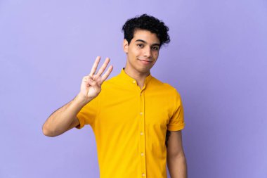 Genç Venezuelalı adam mor arka planda izole edilmiş mutlu ve parmaklarıyla üçe kadar sayıyor.
