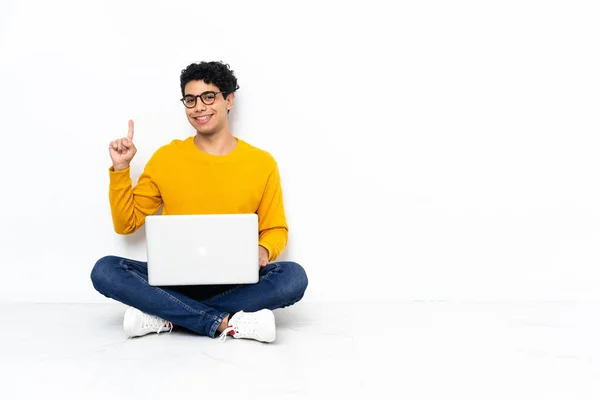委内瑞拉男子坐在地板上 用笔记本电脑展示和举起一个手指 表示最好的迹象 — 图库照片