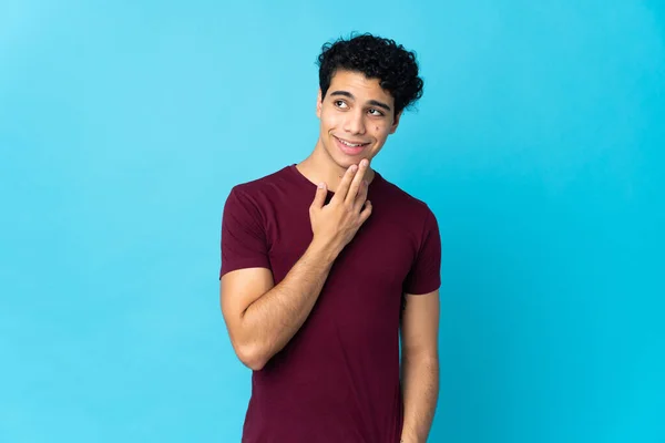 Mladý Venezuelský Muž Izolovaný Modrém Pozadí Vzhlíží Usmívá — Stock fotografie