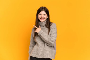 Sarı arka planda izole edilmiş genç Ukraynalı kız bir ürünü sunmak için yan tarafı işaret ediyor.
