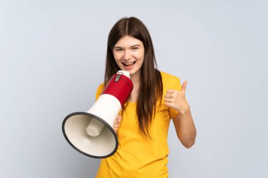 Beyaz arka planda izole edilmiş genç Ukraynalı kız bir şey duyurmak için megafondan bağırıyor ve başparmağını kaldırıyor.