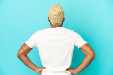 Genç Kolombiyalı yakışıklı adam mavi arka planda izole edilmiş.