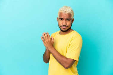 Genç Kolombiyalı yakışıklı adam mavi arka planda bir şeyler planlıyor.