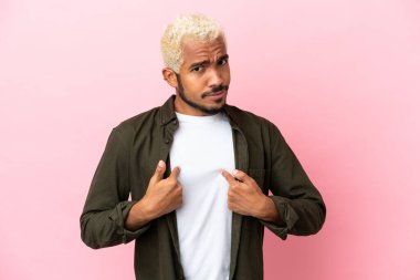 Pembe arka planda izole edilmiş genç Kolombiyalı yakışıklı adam kendini işaret ediyor.