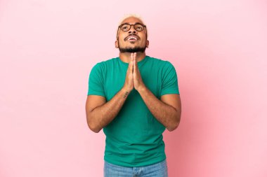 Pembe arka planda izole edilmiş genç Kolombiyalı yakışıklı adam avuç içlerini bir arada tutuyor. İnsan bir şey ister.