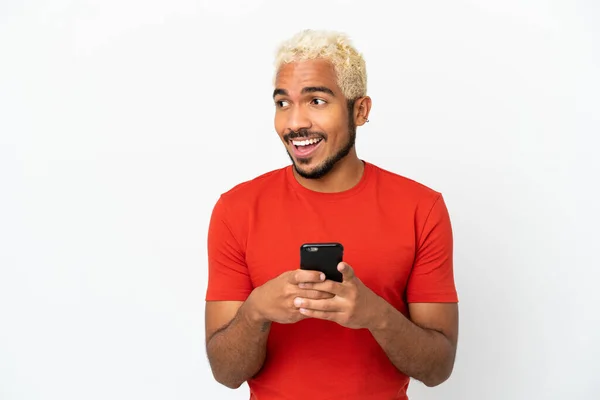 Mladý Kolumbijský Pohledný Muž Izolovaný Bílém Pozadí Pomocí Mobilního Telefonu — Stock fotografie