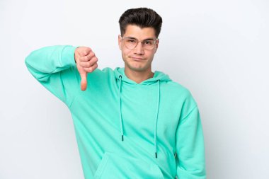 Beyaz bakkalda izole edilmiş genç, yakışıklı beyaz bir adam, olumsuz bir ifadeyle baş parmağını aşağı gösteriyor.