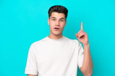 Genç, yakışıklı, beyaz bir adam, mavi bir bakkalda izole edilmiş, parmağını kaldıracak bir fikir düşünüyor.