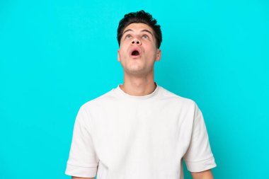 Genç, yakışıklı, beyaz bir adam, mavi bir bakkalda soyutlanmış ve şaşırmış bir ifadeyle yukarı bakıyor.