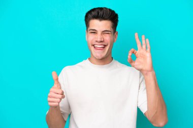 Genç, yakışıklı, beyaz bir adam, mavi bir bakkalda izole edilmiş. Tamam işareti gösteriyor.