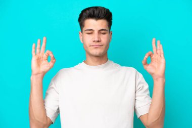 Genç, yakışıklı, beyaz bir adam. Zen pozisyonunda, mavi bir bakkalda izole edilmiş.