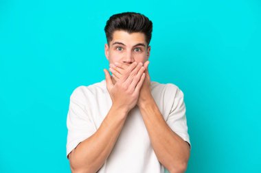 Genç, yakışıklı, beyaz bir adam. Mavi bir bakkalda izole edilmiş. Ağzını elleriyle kapatıyor.