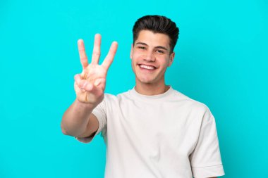 Genç yakışıklı beyaz adam mavi fırında izole edilmiş mutlu ve parmaklarıyla üçe kadar sayıyor.