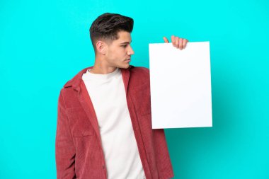 Genç, beyaz, yakışıklı bir adam mavi bir bakkal sahasında izole edilmiş, elinde boş bir levha var ve ona bakıyor.