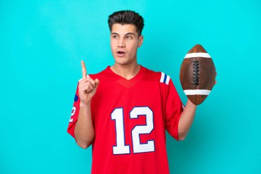 Genç beyaz adam rugby oynuyor. Mavi arka planda izole edilmiş. Parmakla işaret eden bir fikir düşünüyor.