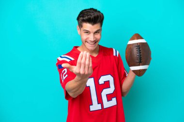 Rugby oynayan Kafkasyalı genç bir adam mavi arka planda izole edilmiş bir şekilde bizimle gelmesi için davet ediyor. Gelmene sevindim.