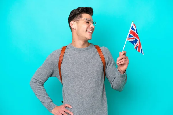 青い背景にイギリス国旗を掲げた若い白人男性が腰で腕を振りながら微笑む — ストック写真