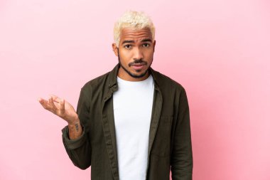 Pembe arka planda izole genç Kolombiyalı yakışıklı adam şüpheli hareketler yapıyor.