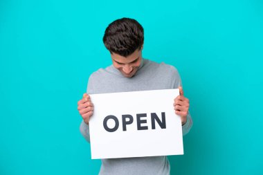 Mavi bakkalda izole edilmiş yakışıklı beyaz bir adam elinde açık metinli bir pankart tutuyor.