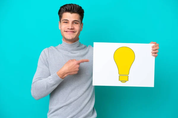 Young Handsome Caucasian Man Isolated Blue Bakcground Holding Placard Bulb — Stock Photo, Image