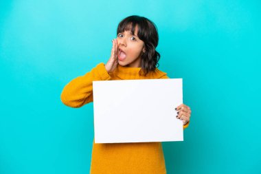 Mavi arka planda izole edilmiş genç Latin bir kadın boş bir levha tutuyor ve bağırıyor.