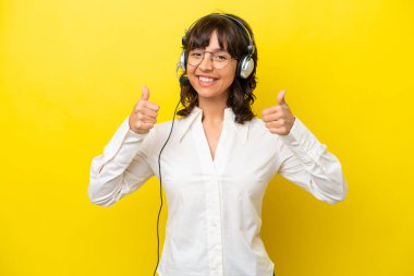 Tele pazarlamacı Latin kadın sarı arka planda izole bir kulaklıkla çalışıyor.