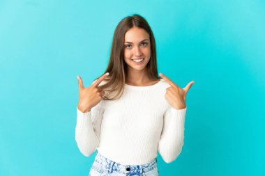 Soyutlanmış mavi arka planda genç bir kadın baş parmak işareti yapıyor.
