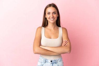 Soyutlanmış pembe arka planda genç bir kadın kollarını ön cephede çapraz tutuyor.