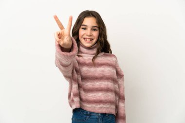 Beyaz arka planda izole edilmiş küçük beyaz kız gülümsüyor ve zafer işareti gösteriyor.