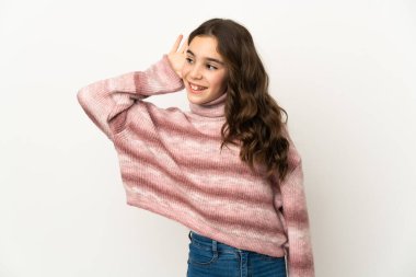 Beyaz arka planda izole edilmiş küçük beyaz kız elini kulağına koyarak bir şeyler dinliyor.