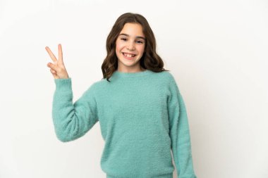 Beyaz arka planda izole edilmiş küçük beyaz kız gülümsüyor ve zafer işareti gösteriyor.