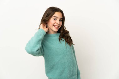 Beyaz arka planda izole edilmiş küçük beyaz kız elini kulağına koyarak bir şeyler dinliyor.