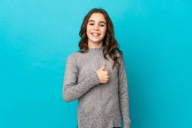 Mavi arka planda izole edilmiş küçük beyaz bir kız baş parmak hareketi yapıyor.
