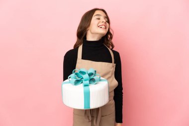 Küçük pasta şefi pembe arka planda izole edilmiş büyük bir pasta tutuyor.