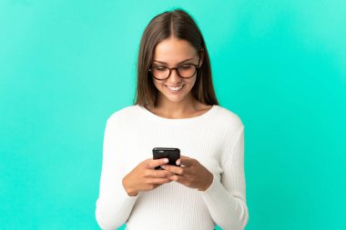 İzole edilmiş mavi arka plan üzerinde genç bir kadın cep telefonuyla bir mesaj ya da e-posta gönderiyor