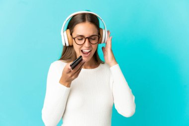 Soyutlanmış mavi arka plan müzik dinleyen ve şarkı söyleyen genç bir kadın.