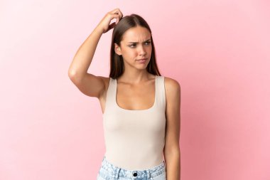 Soyutlanmış pembe arka planı olan genç bir kadın kafasını kaşırken şüpheye düşüyor.