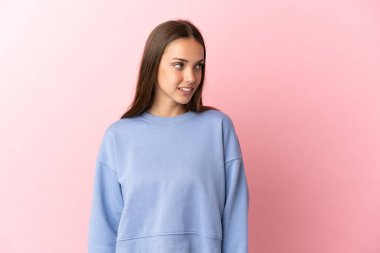 Soyutlanmış pembe arka planı olan genç bir kadın yan tarafa bakıyor.